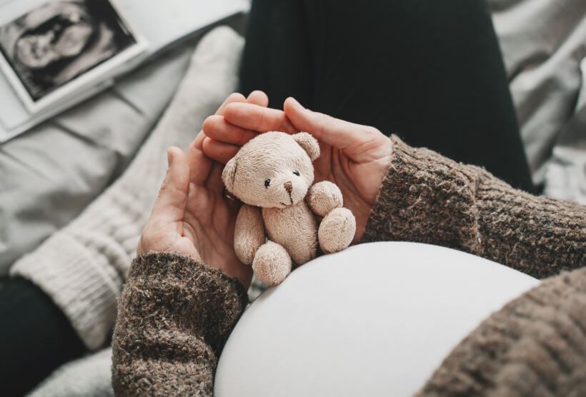 woman holding a teddy bear over her baby bump